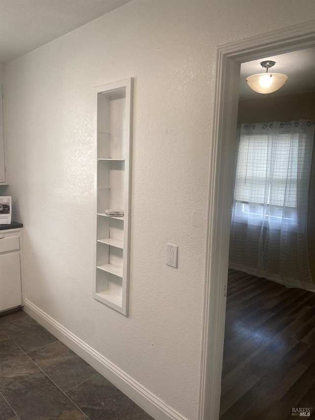 interior space with a textured wall, built in shelves, and baseboards