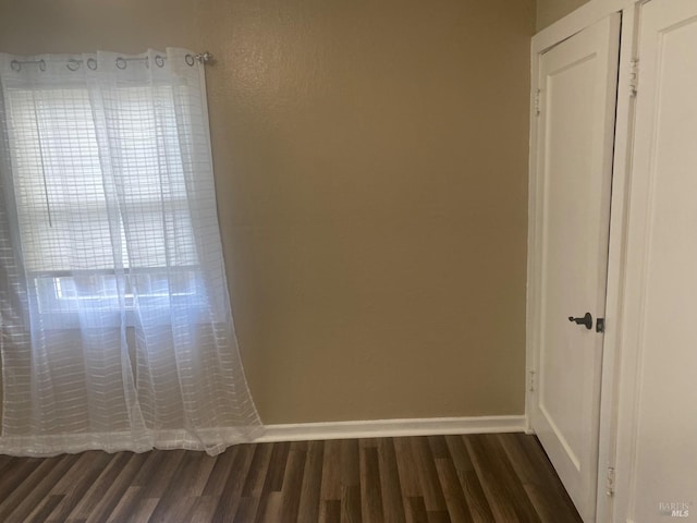 spare room featuring dark wood-type flooring and baseboards