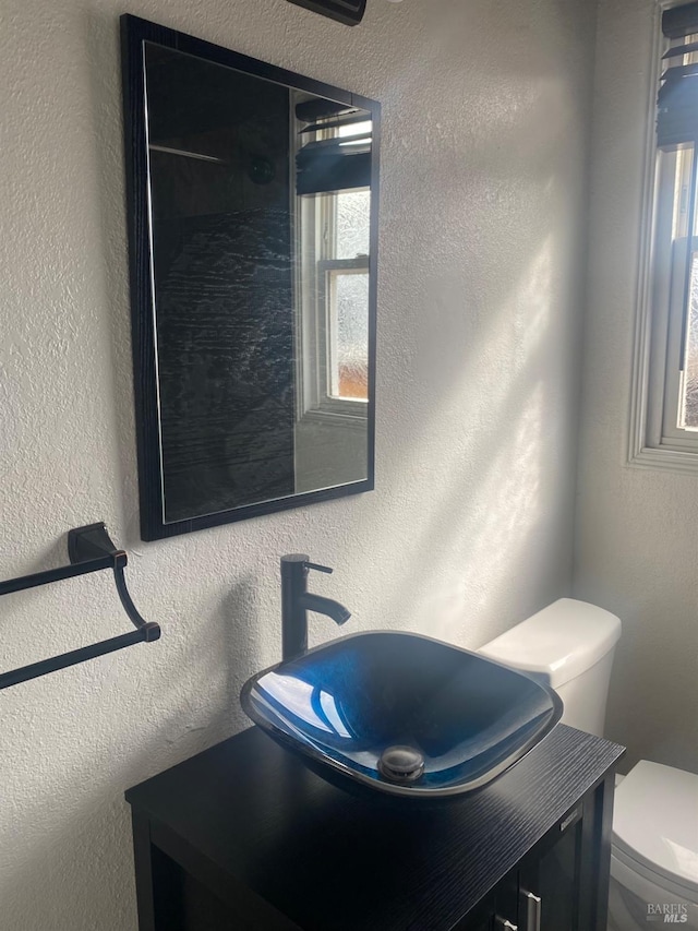 half bathroom featuring toilet, vanity, and a textured wall