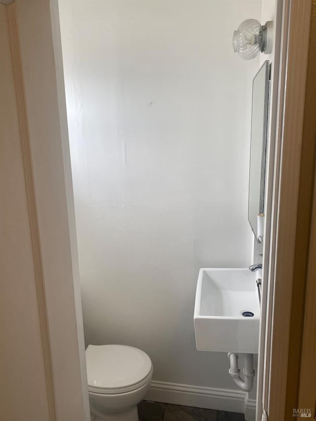 half bathroom with toilet, baseboards, and a sink