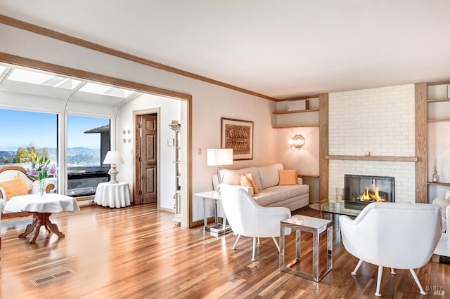 living area featuring visible vents, ornamental molding, a brick fireplace, wood finished floors, and baseboards