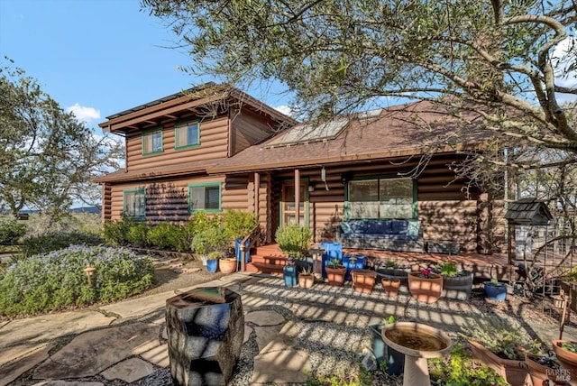 rear view of house featuring roof with shingles, solar panels, outdoor lounge area, a patio area, and log exterior