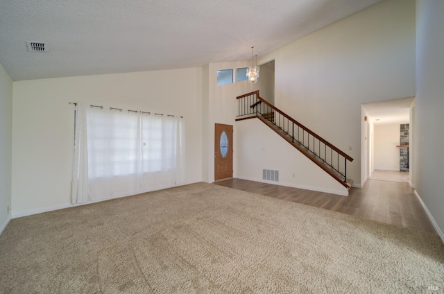 unfurnished living room with high vaulted ceiling, carpet, visible vents, and stairway