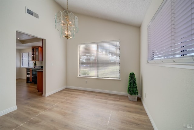 unfurnished dining area with light wood-style flooring, a notable chandelier, visible vents, baseboards, and vaulted ceiling