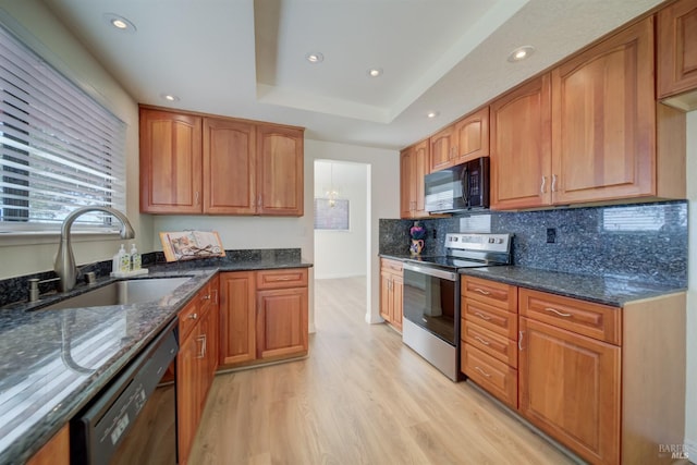 kitchen featuring brown cabinetry, dark stone countertops, a sink, and black appliances