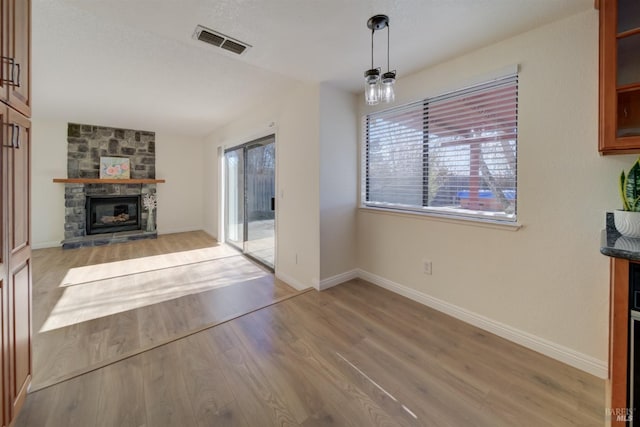 unfurnished living room with light wood-style floors, visible vents, a stone fireplace, and baseboards