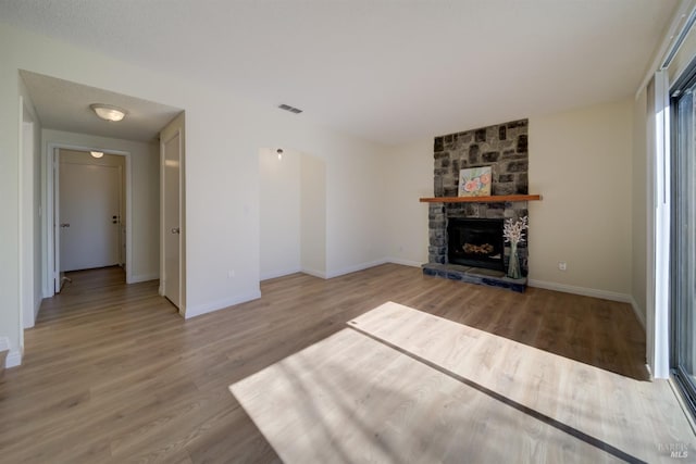 unfurnished living room with a fireplace, wood finished floors, visible vents, and baseboards