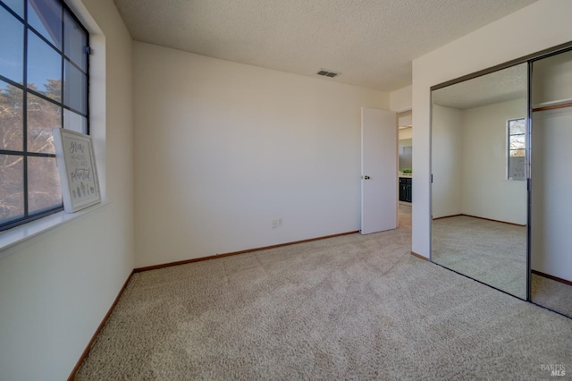 unfurnished bedroom with baseboards, visible vents, light colored carpet, a textured ceiling, and a closet