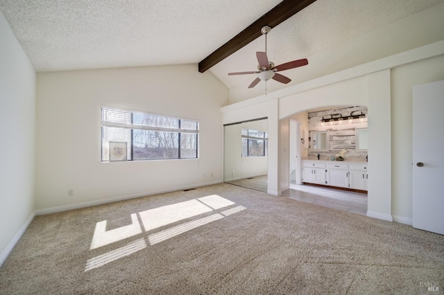 unfurnished bedroom with light carpet, a textured ceiling, arched walkways, and beamed ceiling