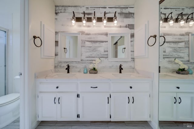 full bath featuring a stall shower, a sink, toilet, and double vanity