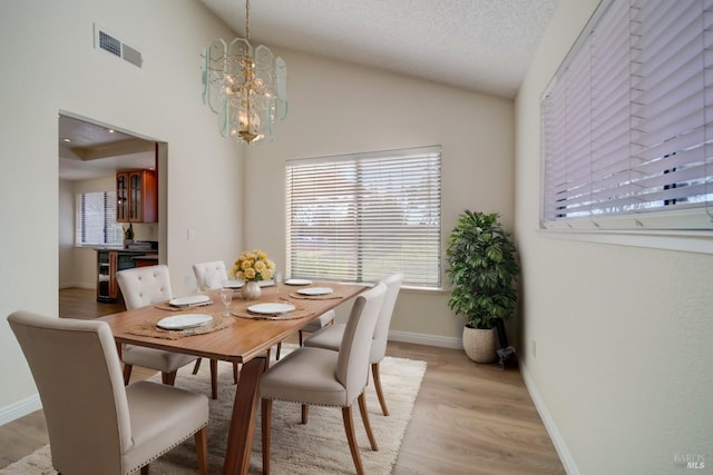 dining area with light wood finished floors, lofted ceiling, visible vents, an inviting chandelier, and a textured ceiling