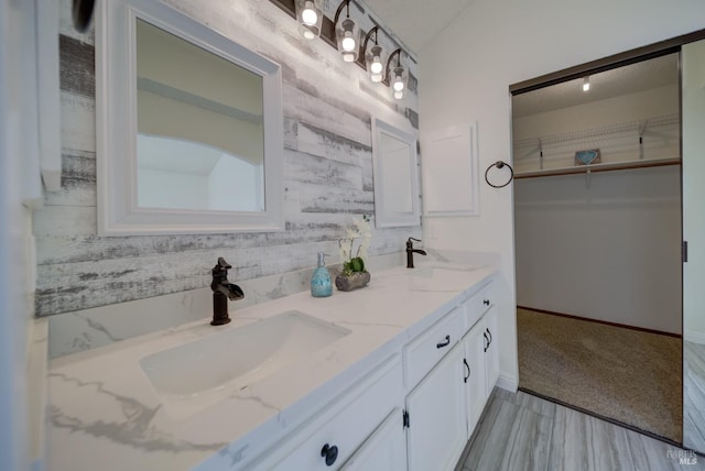 bathroom featuring a spacious closet, double vanity, a sink, and baseboards