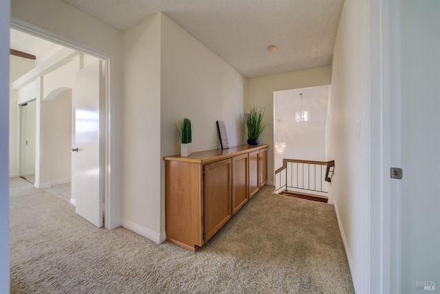 hall featuring light carpet, baseboards, arched walkways, and an upstairs landing