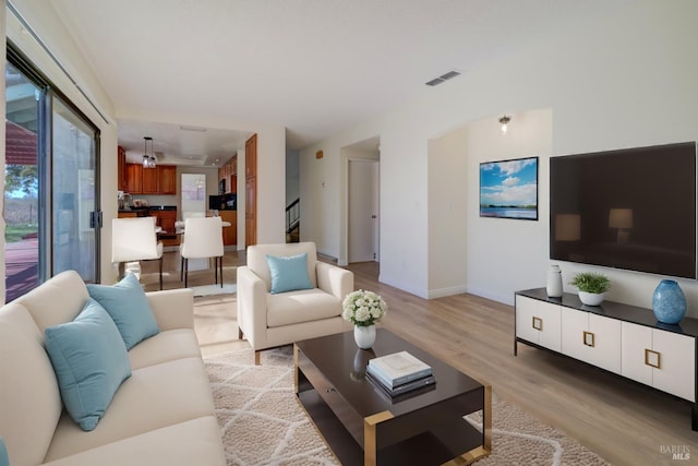 living room featuring light wood-style flooring, stairway, visible vents, and baseboards