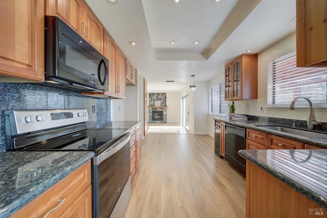 kitchen featuring a sink, light wood-type flooring, black appliances, a raised ceiling, and glass insert cabinets