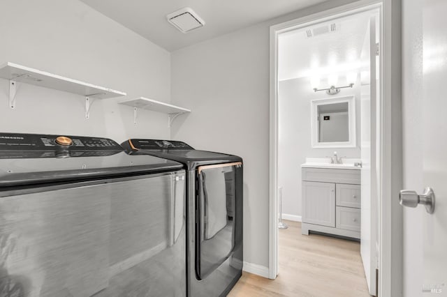 clothes washing area with a sink, light wood-type flooring, laundry area, independent washer and dryer, and baseboards