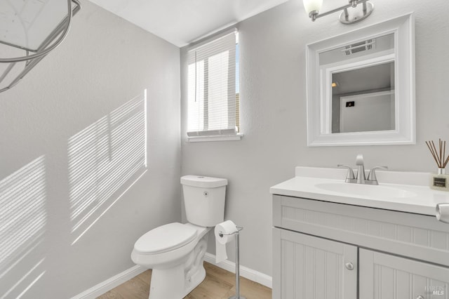 bathroom featuring toilet, wood finished floors, vanity, visible vents, and baseboards