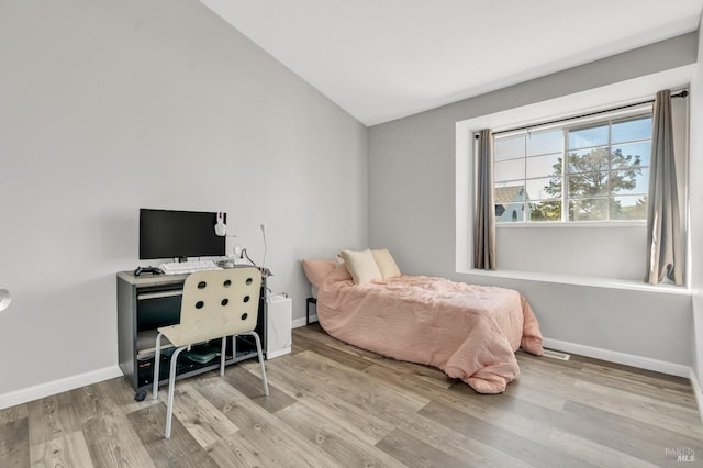 bedroom with vaulted ceiling, light wood-style flooring, and baseboards