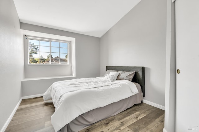 bedroom with vaulted ceiling, baseboards, and wood finished floors