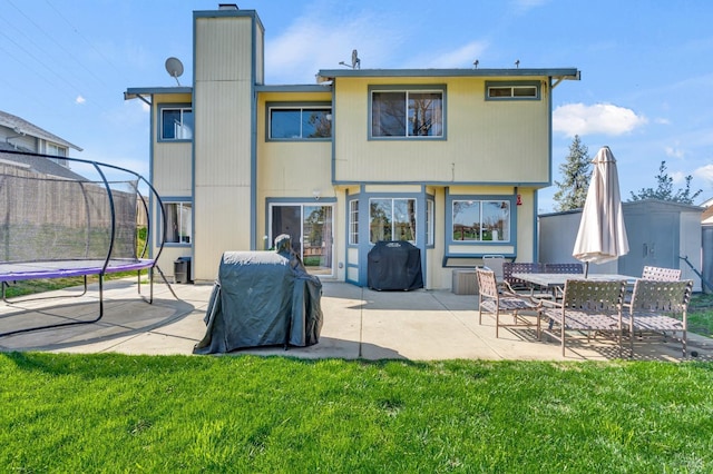 rear view of house featuring a trampoline, a patio area, and a lawn