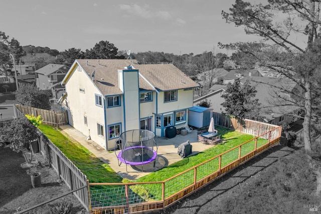 rear view of house with a trampoline, a patio area, a fenced backyard, and a chimney