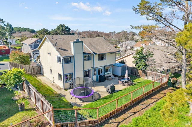 rear view of property with a fenced backyard, a trampoline, a residential view, and a chimney