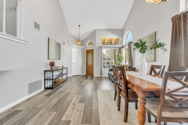 dining room featuring light wood finished floors, baseboards, visible vents, and high vaulted ceiling