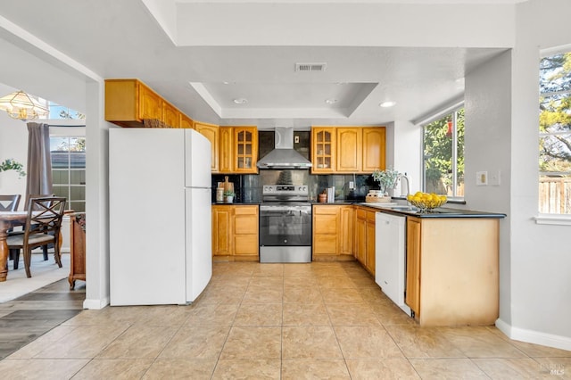 kitchen with white appliances, visible vents, dark countertops, a tray ceiling, and wall chimney range hood