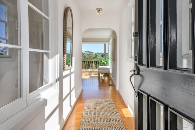 entryway featuring arched walkways, baseboards, and light wood-style floors