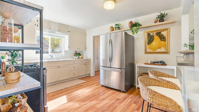 kitchen with stainless steel appliances, a sink, white cabinetry, light countertops, and light wood-type flooring