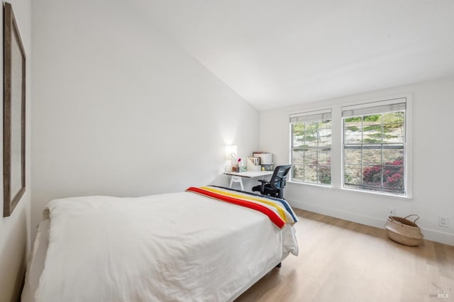 bedroom featuring baseboards, vaulted ceiling, and light wood finished floors