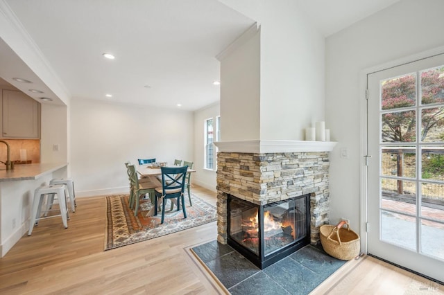 dining room with baseboards, ornamental molding, a stone fireplace, light wood-style floors, and recessed lighting