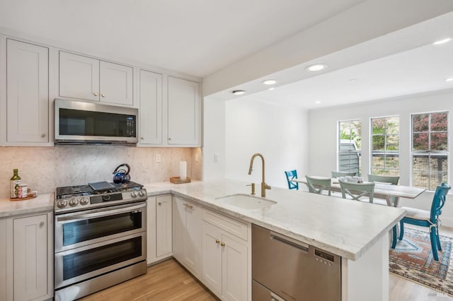 kitchen featuring a peninsula, light stone countertops, stainless steel appliances, white cabinetry, and a sink