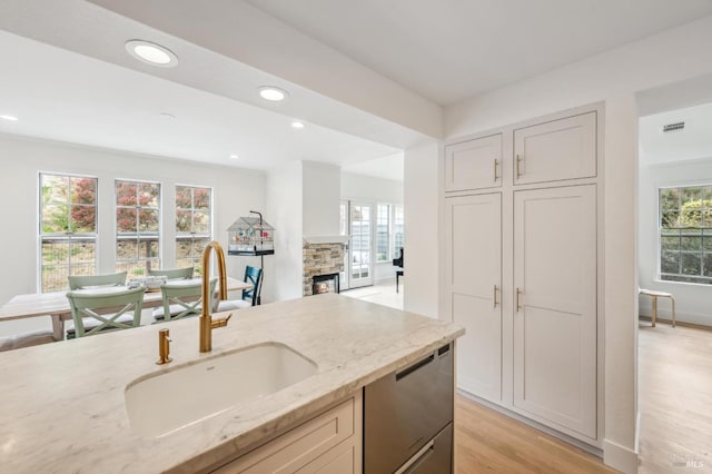 kitchen with light stone counters, a fireplace, light wood-style flooring, stainless steel dishwasher, and a sink