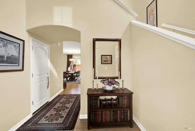 corridor with baseboards, arched walkways, and wood finished floors