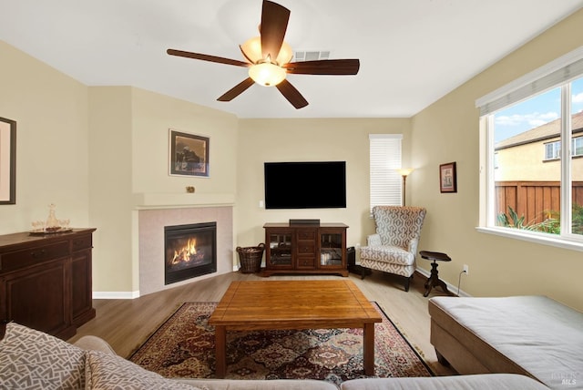 living area featuring a wealth of natural light, visible vents, a tiled fireplace, and wood finished floors