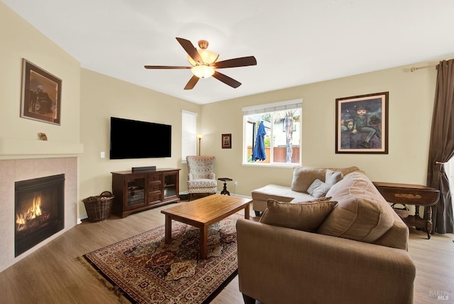 living area featuring ceiling fan, light wood-type flooring, and a tile fireplace