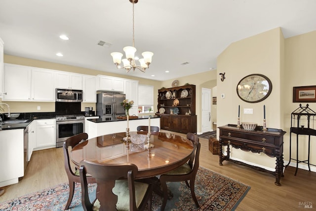 dining room with arched walkways, light wood-type flooring, visible vents, and an inviting chandelier