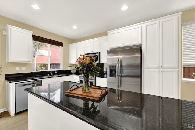 kitchen with stainless steel appliances, recessed lighting, white cabinetry, a sink, and dark stone countertops