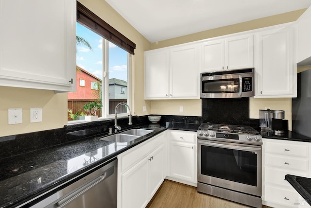 kitchen featuring stainless steel appliances, dark stone counters, white cabinetry, and a sink