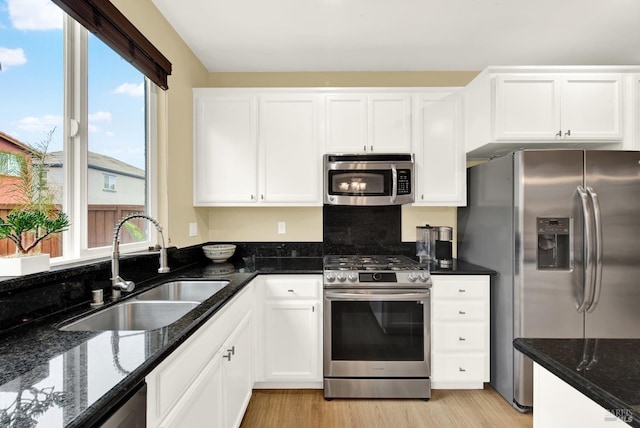 kitchen with light wood-style flooring, a sink, white cabinetry, appliances with stainless steel finishes, and dark stone counters