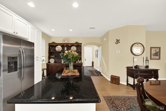 kitchen with arched walkways, dark stone counters, white cabinetry, light wood-type flooring, and stainless steel fridge with ice dispenser