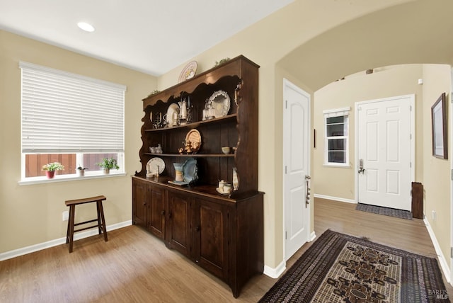 corridor featuring arched walkways, baseboards, light wood finished floors, and recessed lighting