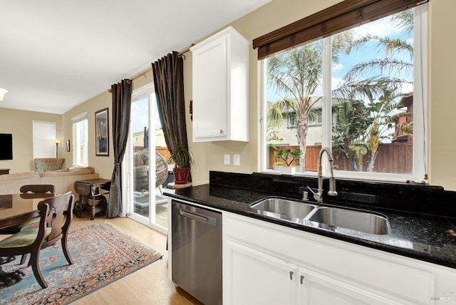 kitchen featuring light wood finished floors, white cabinets, a sink, dark stone countertops, and dishwasher