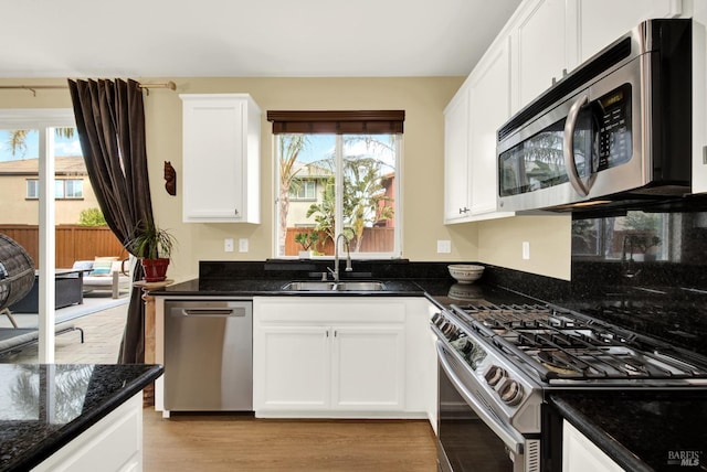 kitchen with light wood-style flooring, appliances with stainless steel finishes, white cabinetry, a sink, and dark stone counters