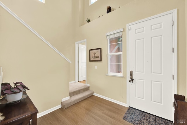 entrance foyer featuring light wood-type flooring, stairs, baseboards, and a high ceiling