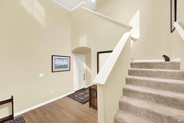 stairway with crown molding, a towering ceiling, baseboards, and wood finished floors