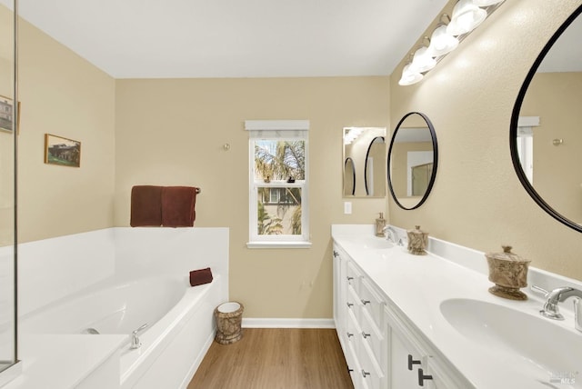 full bathroom with a garden tub, double vanity, wood finished floors, and a sink