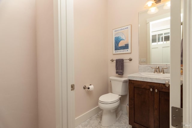 bathroom with toilet, vanity, marble finish floor, and baseboards