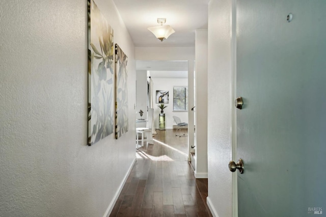 hall with a textured wall, baseboards, and wood finished floors